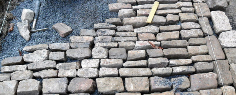 Legung von Natursteinpflaster. Als Richtung dienen aufgespannte Fäden. Pflasterarbeiten gehören zu klassischen Arbeiten im Garten- und Landschaftsbau.