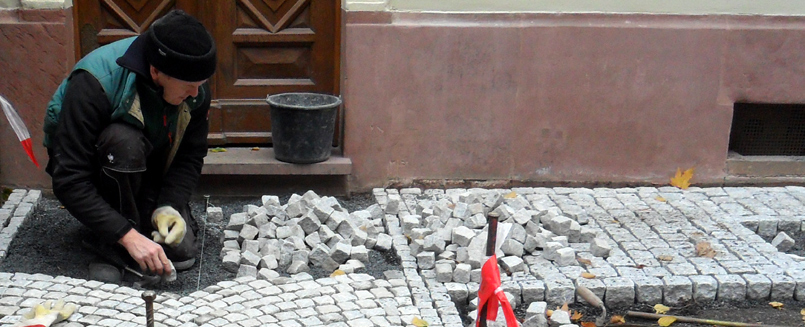 Ein Gartenbauhelfer legt Natursteinpflaster über feinen Kies. Ein Weg wird gestaltet.