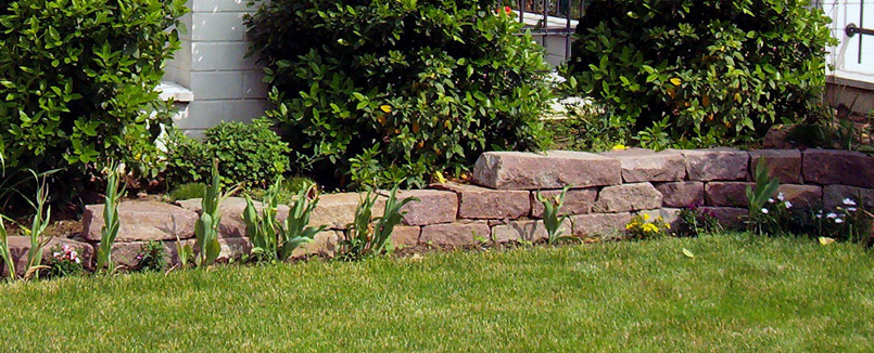 Trockenmauer aus Porphyr-Mauerblöcken als Beeteinfassung in der Gartengestaltung