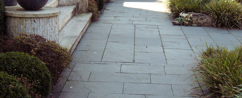 Gestaltung eines Vorgartens: Drei Wege verlegt mit Natursteinplatten aus Schiefer treffen sich an einer dreistufigen Treppe. 
